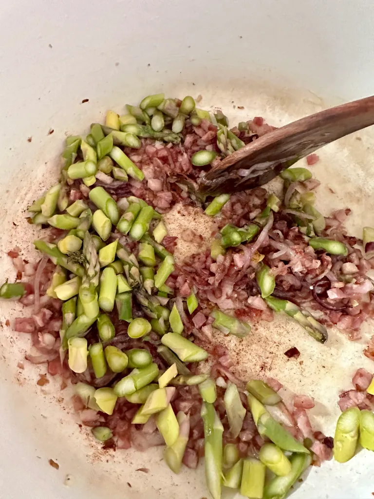 Adding sliced asparagus to browned pancetta and onions with wooden spoon