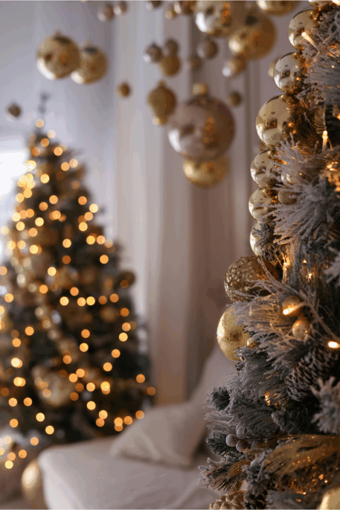 Cozy holiday scene featuring two Christmas trees decorated with gold ornaments and warm string lights, with frosted branches and hanging baubles creating a soft, glowing atmosphere.
