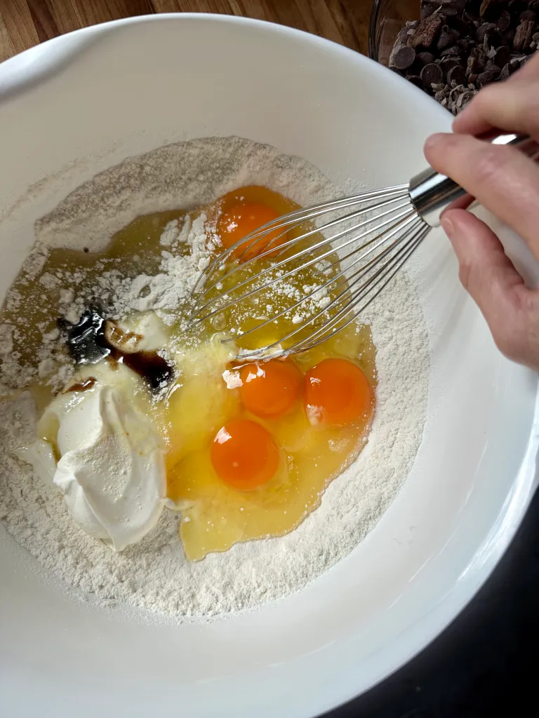 Adding eggs, sour cream, oil, and vanilla to cake mix with a whisk