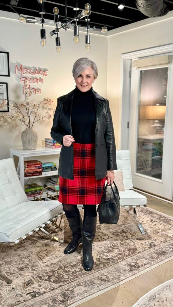 Woman over 50 wearing red tartan plaid skirt with black leather blazer, black turtleneck, tights, and tall black riding boots for Ralph Lauren Christmas style
