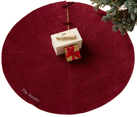 Deep red quilted velvet Christmas tree skirt with subtle stitched texture, shown beneath a lit tree with wrapped gifts placed on top.