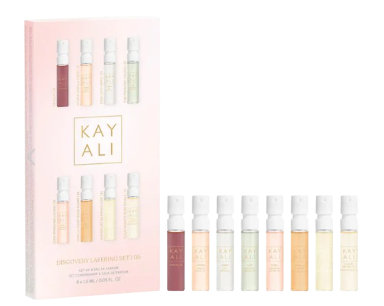 KAYALI Discovery Layering Set with eight mini spray perfumes in pastel-colored bottles lined up beside a pink gradient gift box.