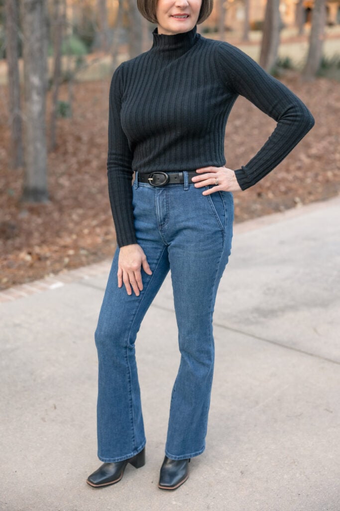 Detail shot of Ann Taylor petite bootcut jeans showing subtle flare at ankle with black heeled boots - classic petite denim fit
