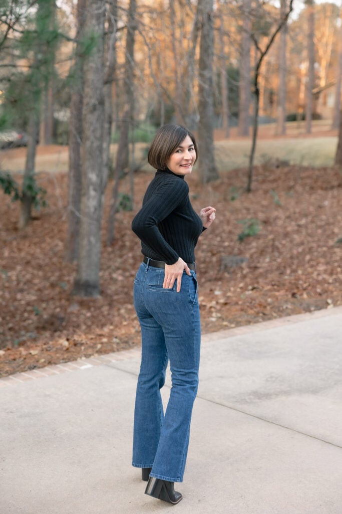 Kelly looking back over shoulder in petite bootcut jeans showing back pocket placement and elongating bootcut hem with black boots