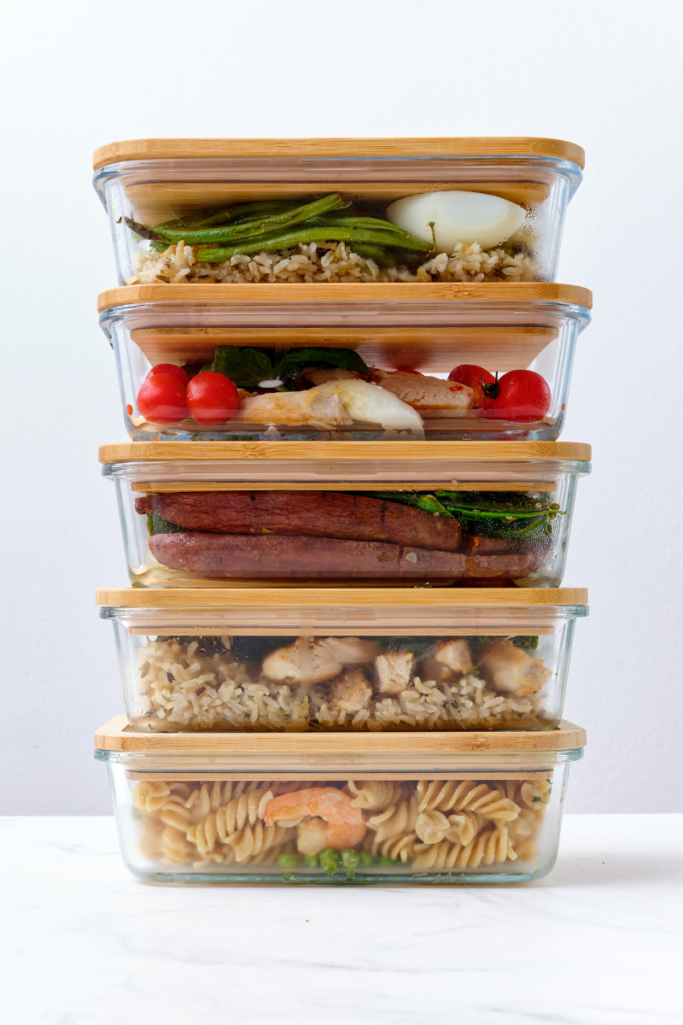 Stack of glass meal prep containers filled with cooked pasta, rice, chicken, vegetables, and shrimp, neatly layered to showcase organized food storage and weekly meal prep.