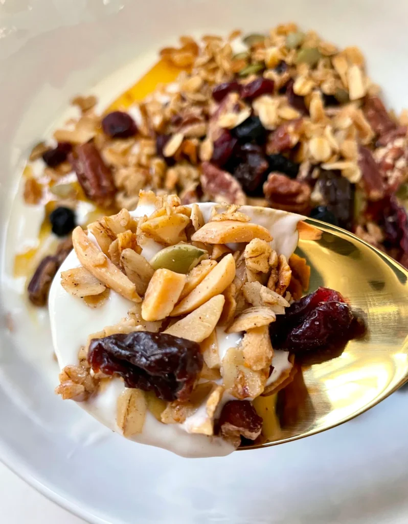 Spoonful of homemade granola with yogurt, dried cherries, cranberries, and almonds on a gold spoon