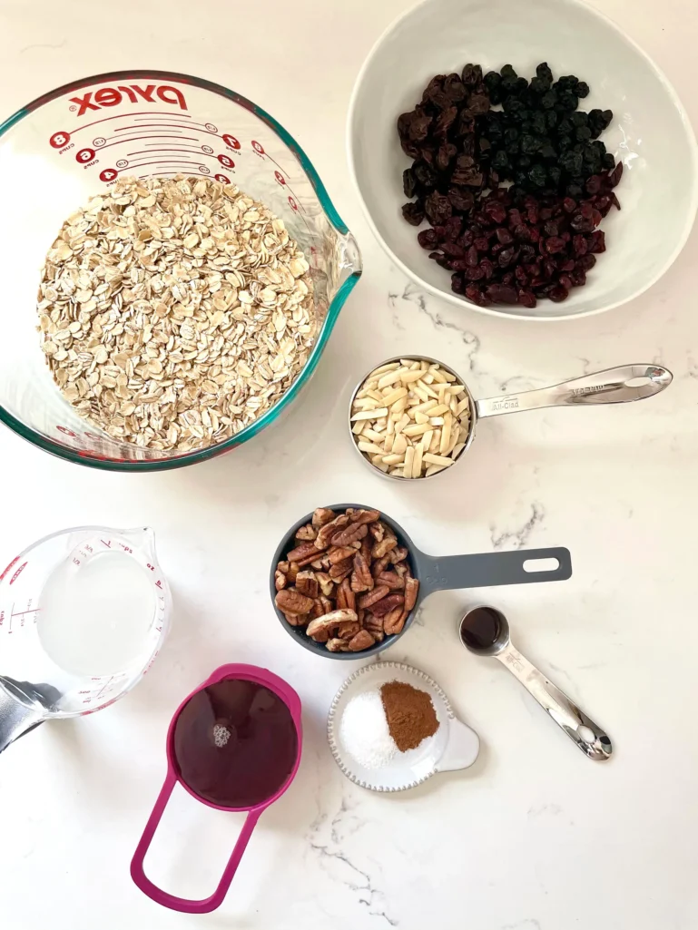 Ingredients for homemade granola: oats, pecans, almonds, dried fruit, maple syrup, coconut oil, cinnamon, salt, and vanilla