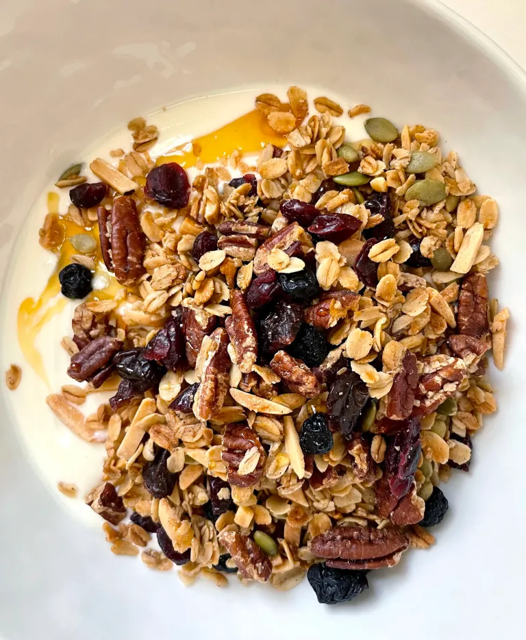 Bowl of yogurt topped with homemade granola and a drizzle of honey