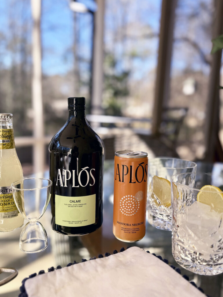 Aplos mocktail ingredients including Aplos Calme bottle, Aplos Mandora Negroni can, Fever-Tree Sparkling Sicilian Lemonade, and crystal rocks glasses with ice and lemon