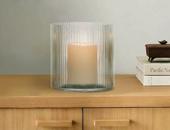 Green ribbed glass candle holder with a white pillar candle, styled on a wood console with books.