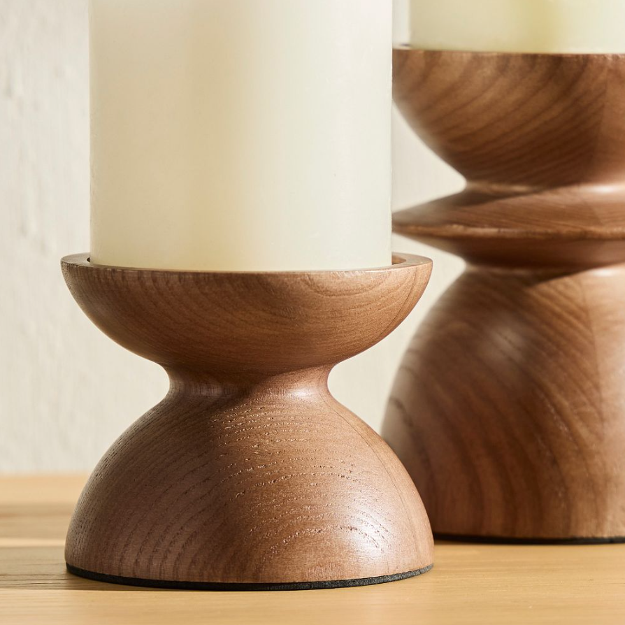 Wood pillar candle holders with rounded, hourglass silhouettes, holding ivory candles and styled on a wooden surface for a warm, organic look.