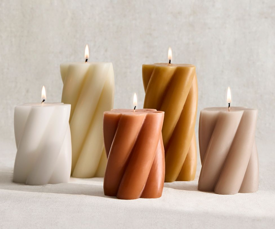 Set of twisted pillar candles in neutral tones, including ivory, tan, and warm brown, lit and arranged together for a modern, sculptural candle display.