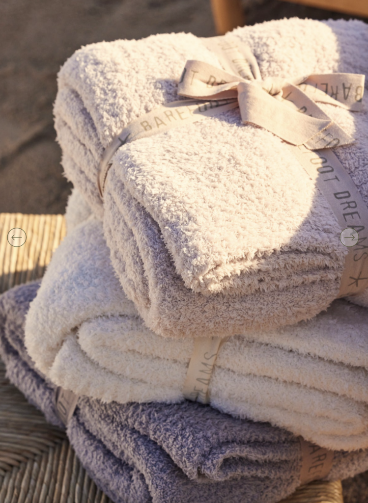 Barefoot Dreams CozyChic throw blanket folded and stacked in neutral cream and soft gray tones, highlighting the plush, cozy knit texture.
