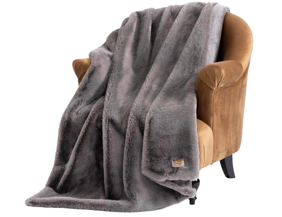 UGG Euphoria plush faux fur throw blanket in soft gray, draped over a camel velvet armchair, showing thick, ultra-cozy texture and generous size.