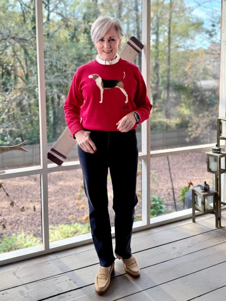 Woman over 50 in white button-up layered under red dog sweater with navy jeans and suede loafers