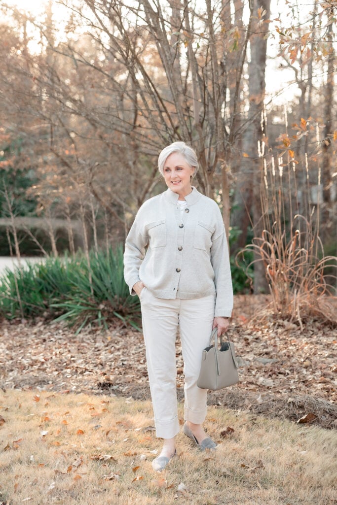 Woman over 50 wearing white tee with cream button cardigan, white chinos, and pointed toe loafers