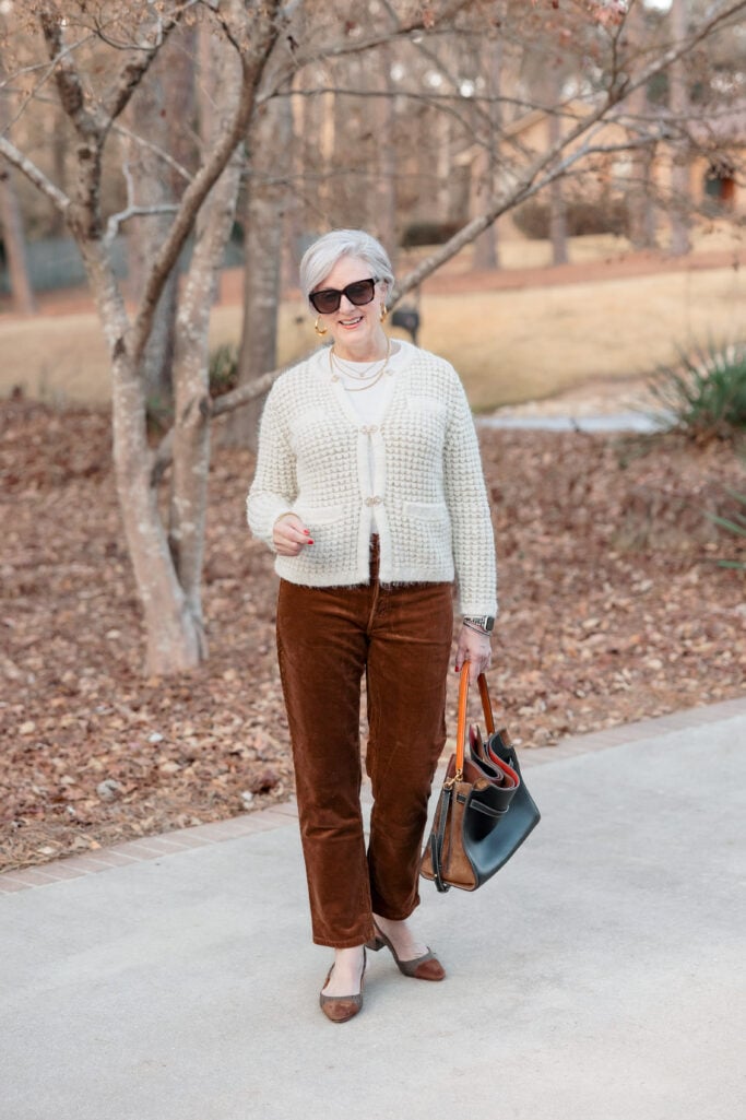 Woman over 50 in white tee layered under textured metallic cardigan with corduroy pants and tweed slingbacks
