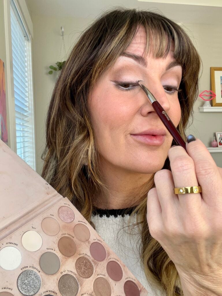 Woman applying white and ivory eyeshadow to inner corner of eye with small brush while holding Colourpop Stone Cold Fox neutral eyeshadow palette