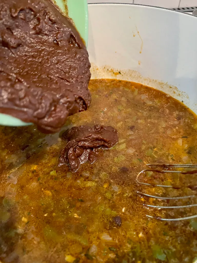 Pouring the roux paste from the mixing bowl into the Dutch oven of gumbo
