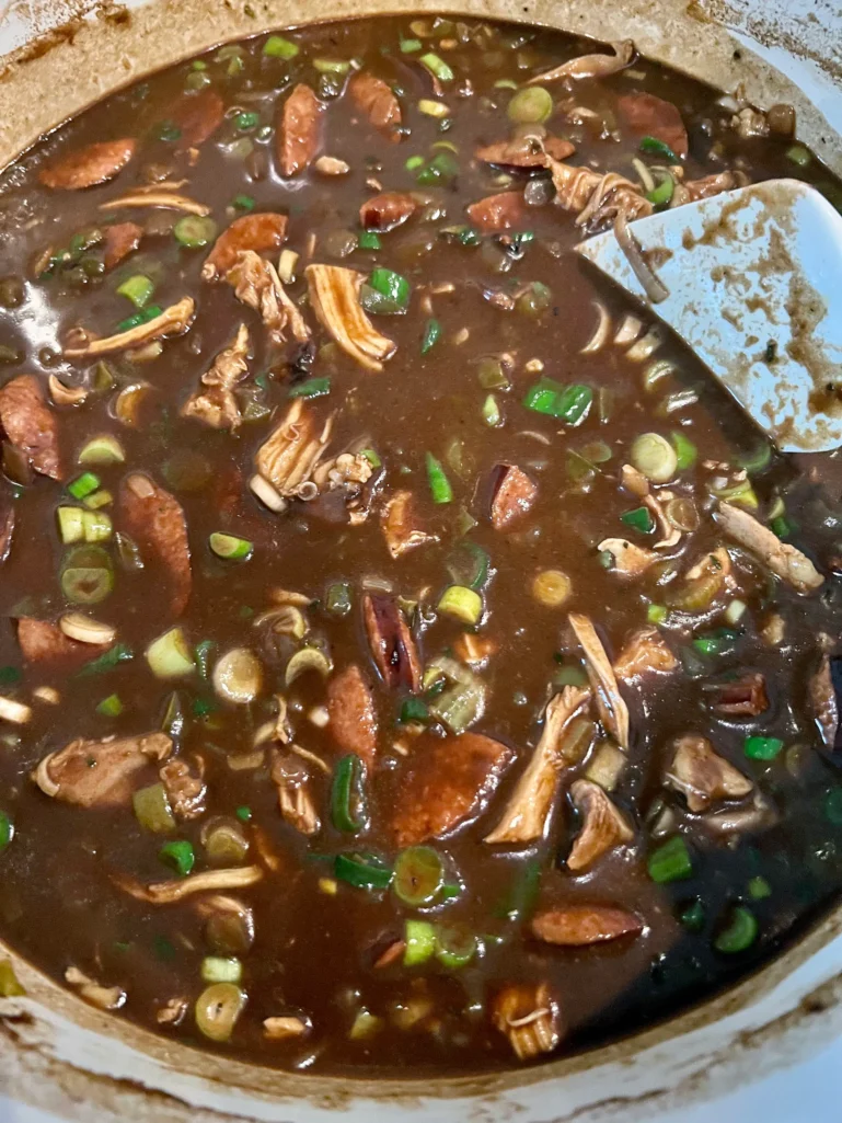 Overhead view of finished gumbo in the Dutch oven with chicken, sausage, and scallions