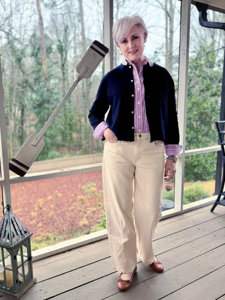 Beth wearing a navy cardigan over a lavender striped button-up, cream wide-leg pants, and cognac ballet flats on the screened porch