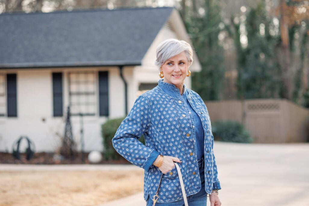 Woman over 50 wearing denim on denim outfit with quilted block-print jacket and gold accessories