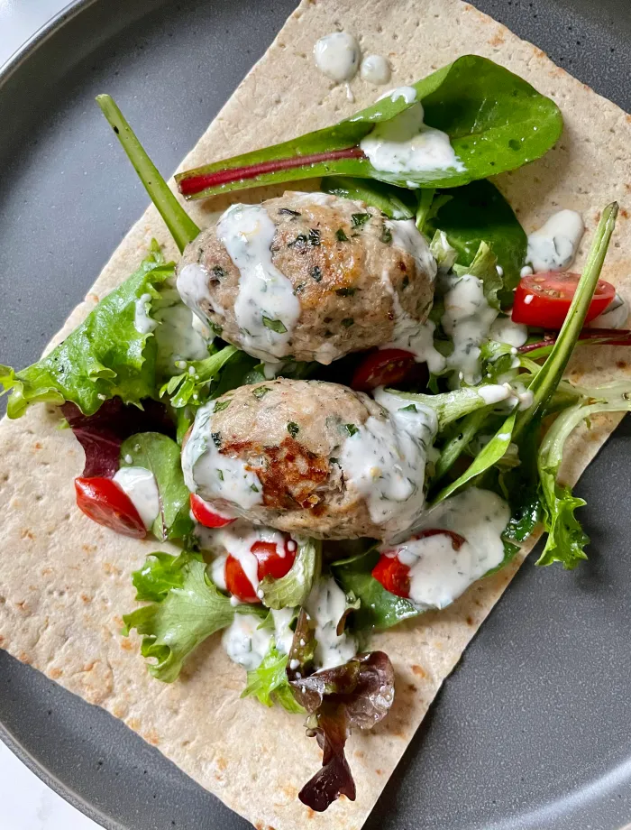 Overhead view of chicken kofta wrap with mixed greens, grape tomatoes, and yogurt sauce on lavash flatbread on a gray plate