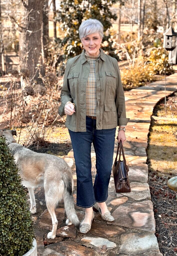 Beth Djalali styling a green utility jacket over a plaid top with dark straight-leg jeans, plaid flats, and a brown leather bag