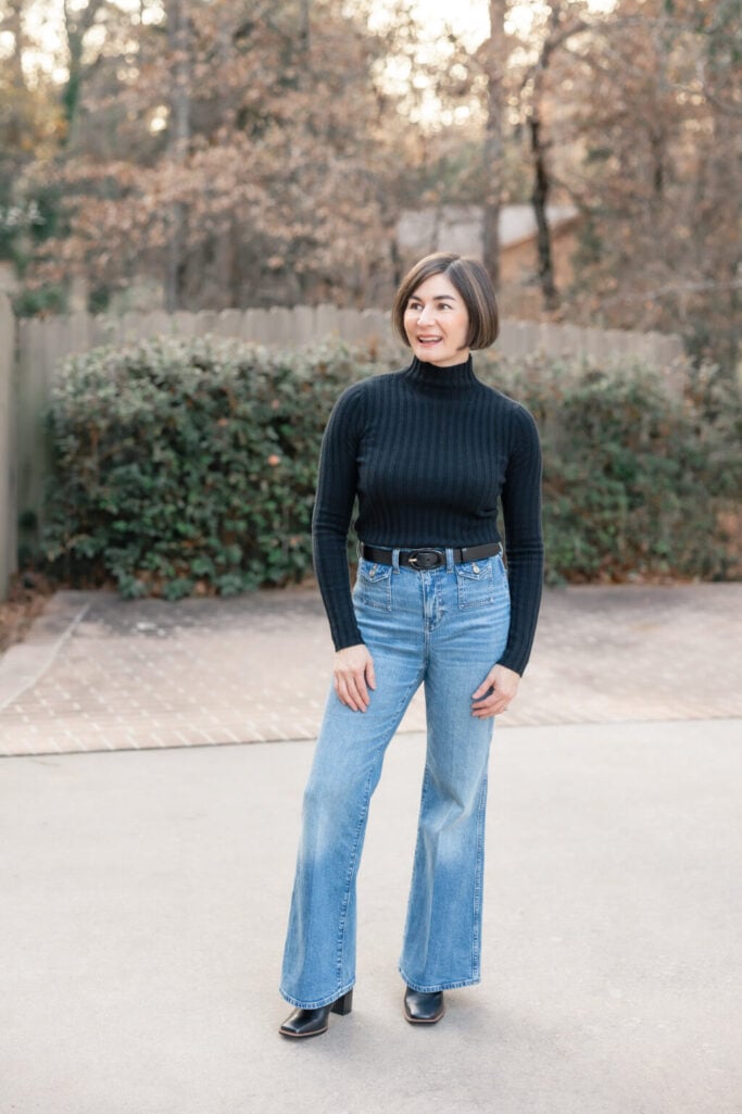 Woman with brown bob haircut wearing black ribbed turtleneck tucked into light wash high-rise wide-leg jeans with black leather belt, black square-toe ankle boots