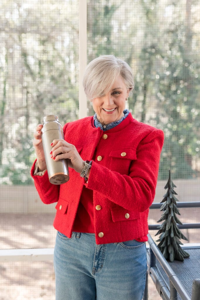 Beth wearing a red tweed jacket with gold buttons over a chambray shirt and jeans, holding a cocktail shaker — red lady jacket outfit idea