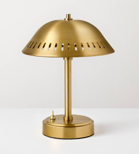 Small portable brass table lamp with a dome-shaped shade and perforated detailing, styled on a tabletop with a warm ambient glow.