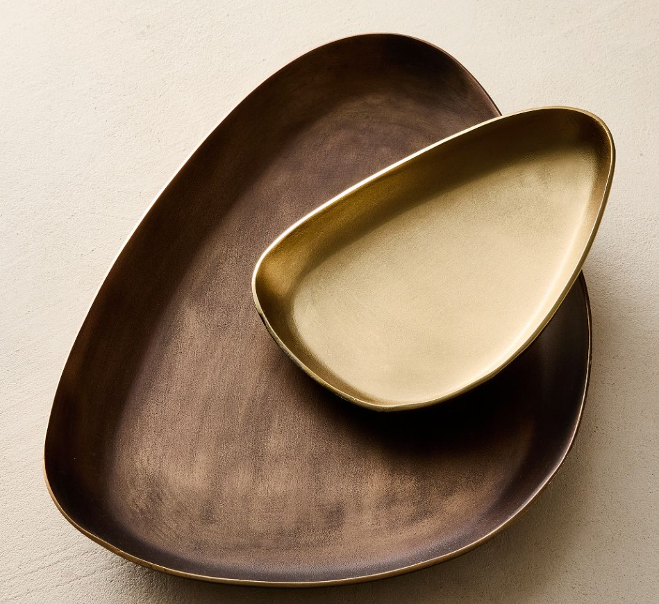 Two organic-shaped metal trinket trays in warm brass and bronze tones, stacked together with softly curved edges and a matte finish.