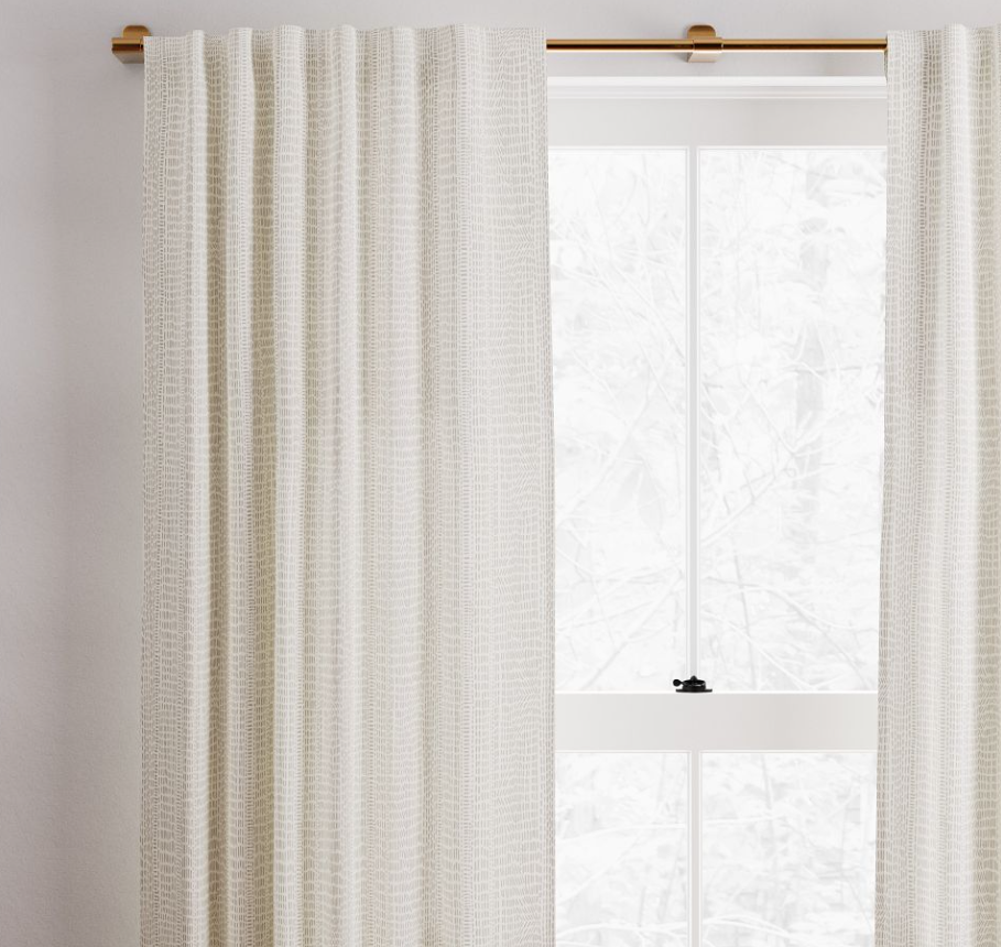Floor-length ivory cotton canvas curtains with a soft woven texture, hanging from a brass curtain rod and filtering natural light through a window.