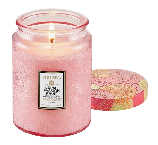 Voluspa Napali Passion Fruit candle in a textured pink glass jar with an embossed pattern, shown lit beside its decorative matching lid. Features a tropical-inspired design and soft ambient glow.