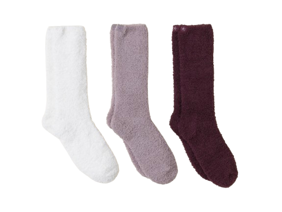 Three pairs of Barefoot Dreams CozyChic socks laid flat in white, soft lavender, and deep burgundy. Plush, fuzzy texture designed for warmth and comfort, ideal for lounging at home.