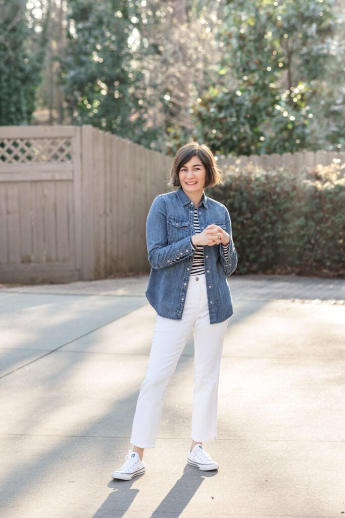 Kelly layering a denim western shirt over a striped Breton tee with white jeans and white Converse — effortless petite spring style