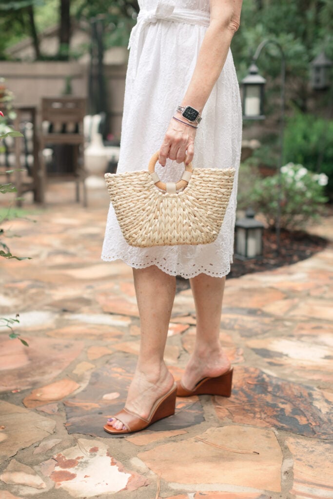 Woman wearing white eyelet midi dress with cognac leather wedge sandals and woven straw tote bag with wrapped handles
