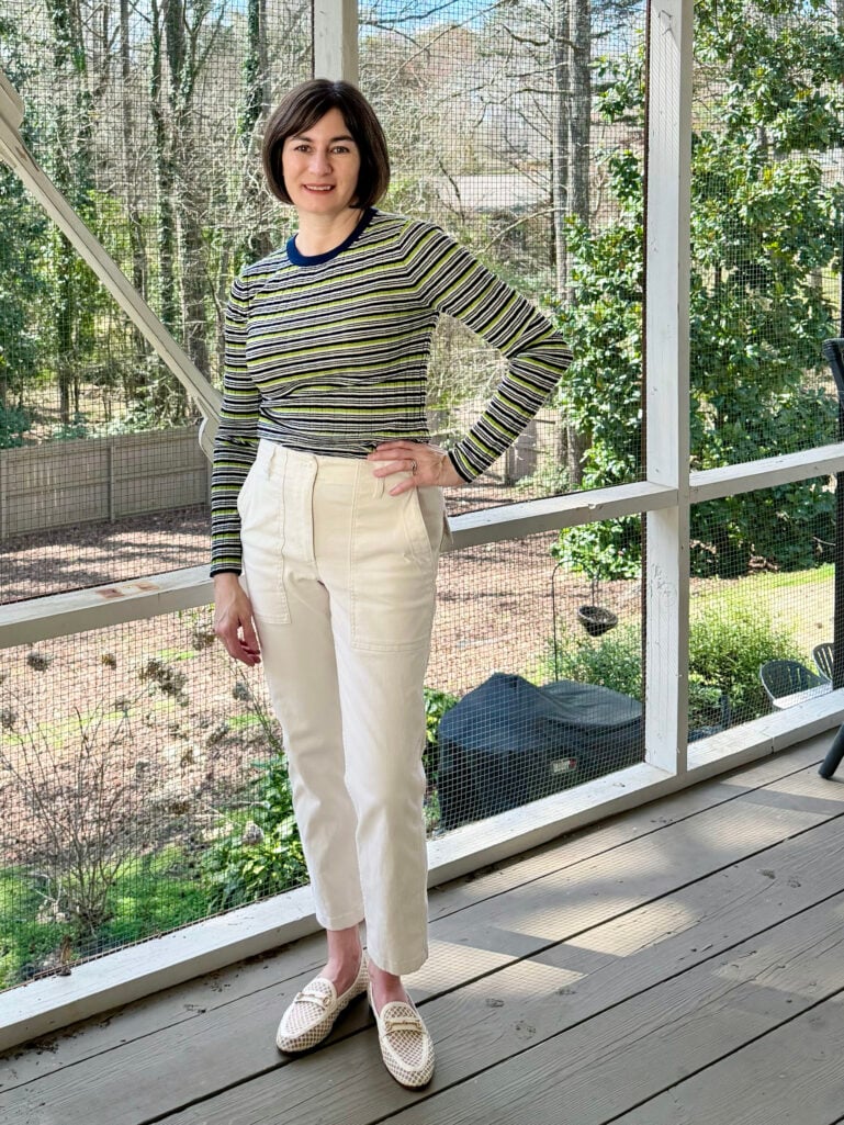 Kelly wearing a green, navy, and white Striped Carolyn Crewneck Sweater with a navy contrast neckline, cream Petite Patch Pocket Slim Chino Pants, and Loraine Mesh Bit Loafers on the screened porch