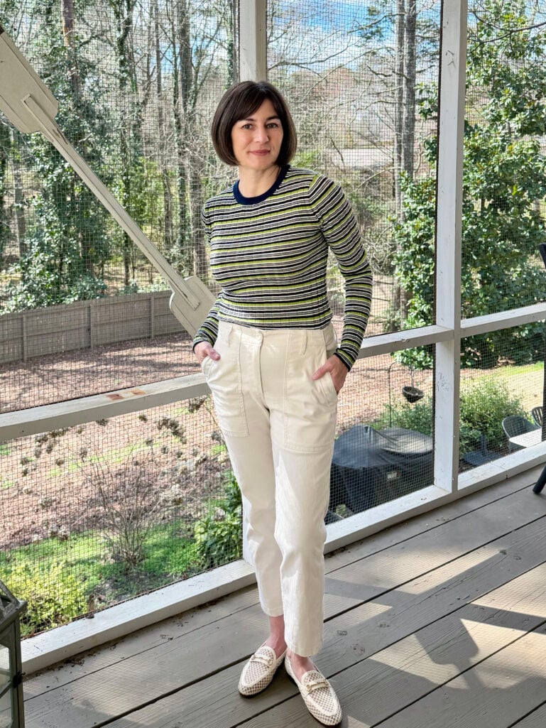 Full-length view of Kelly in her striped crewneck and cream chinos, hands in pockets, smiling in the spring light on the porch