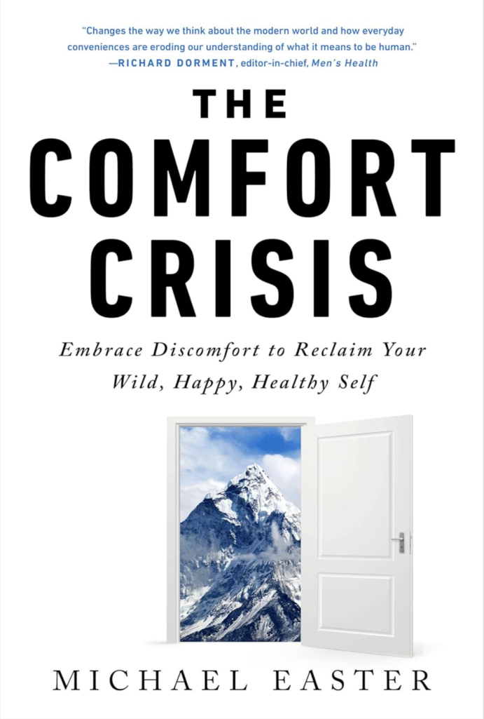 Book cover of The Comfort Crisis by Michael Easter featuring bold black typography and an image of an open door revealing a snowy mountain landscape, symbolizing stepping outside comfort zones.