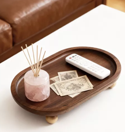 Acacia wood decorative tray with raised edges and small feet, styled with a reed diffuser, remote control, and vintage-style paper accents.