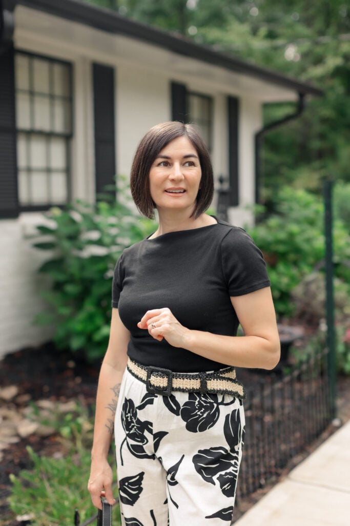Woman with brown bob wearing fitted black crewneck tee with cream and black floral wide-leg linen pants, striped woven raffia belt in black and natural
