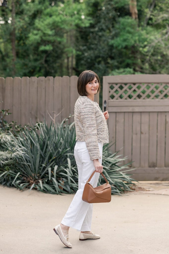 Back view of Kelly in cream Italian textured tweed lady jacket with white straight-leg linen trousers and cognac leather bag — petite spring outfit styling