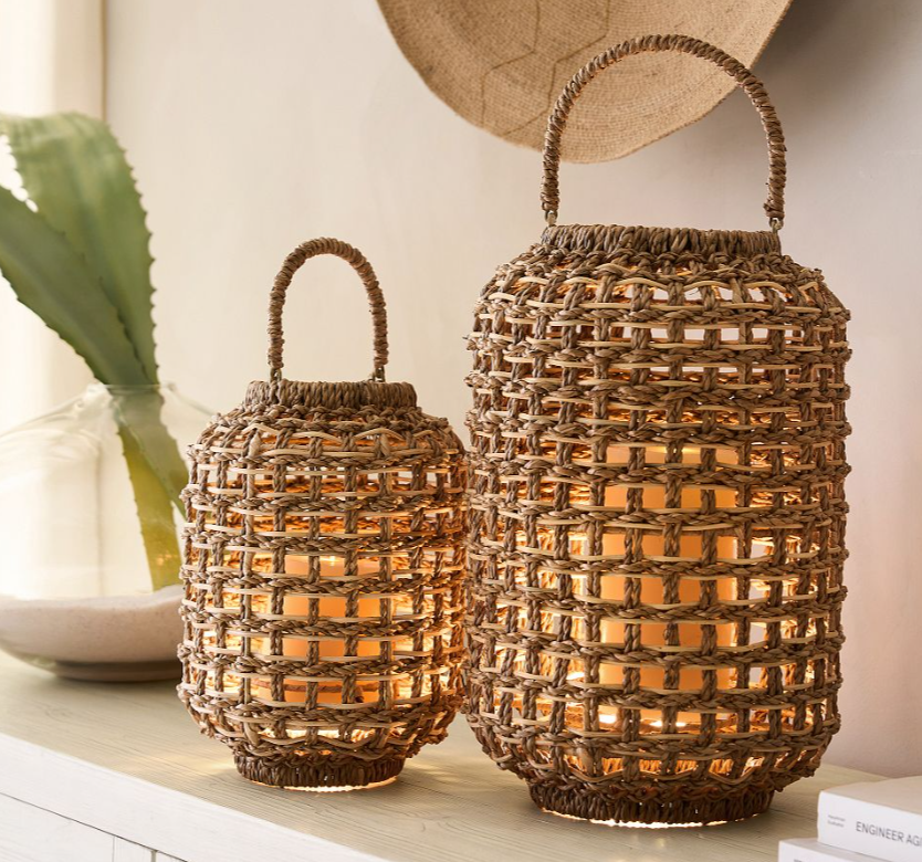 Set of two woven rattan lanterns with loop handles, glowing warmly with candles inside for a cozy indoor or outdoor ambiance.