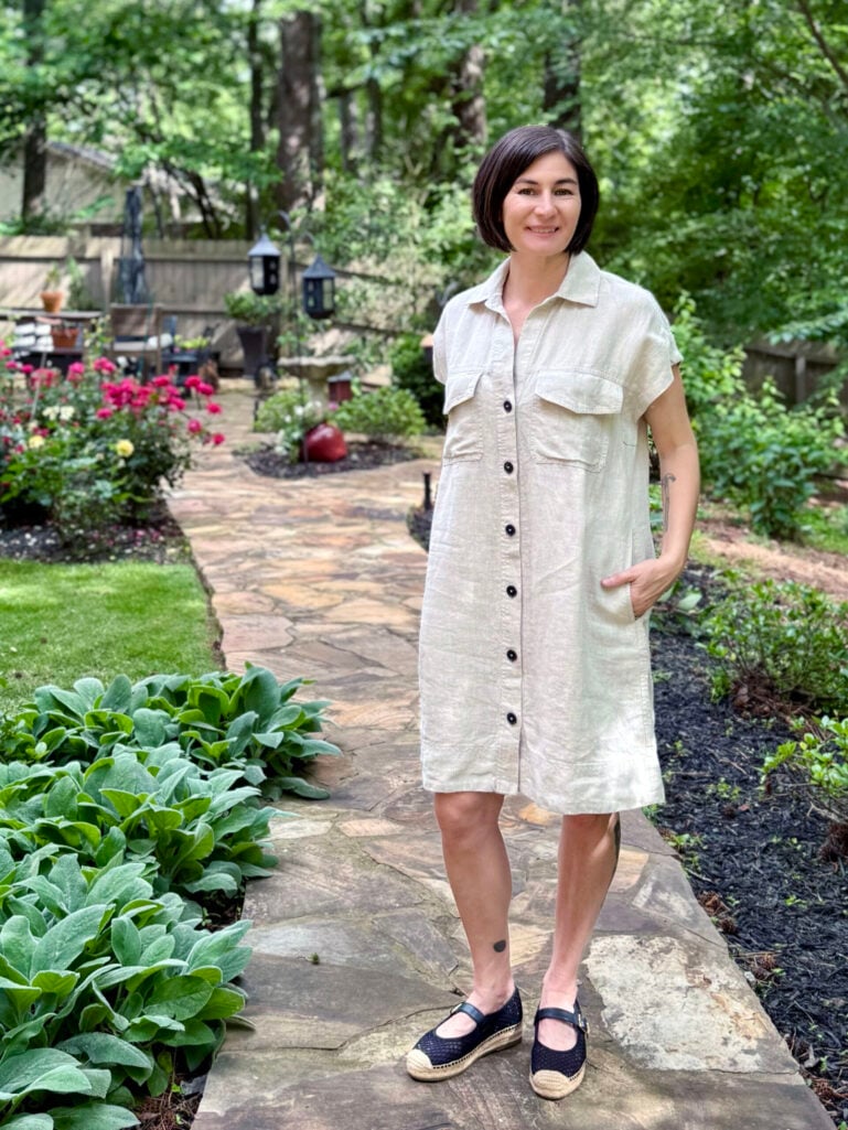 Kelly in natural linen shirtdress worn loose with black espadrille flats in garden setting — casual petite shirtdress summer outfit