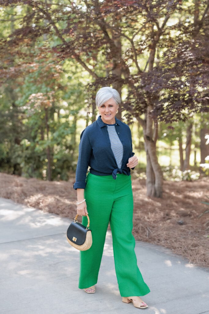 Summer 2026 colors after 50 — woman wearing kelly green wide-leg linen pants with navy linen shirt knotted over a striped tee and rattan handbag