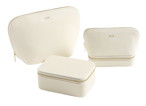 Set of three cream leather travel pouches with gold zippers and monogram initials, in large, medium, and rectangular shapes for makeup and accessories.