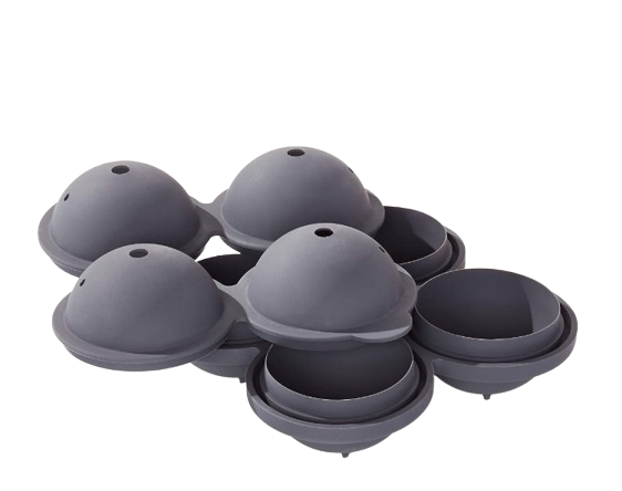 Dark gray silicone ice tray mold designed to create large round ice spheres beside a whiskey glass on a white tabletop.