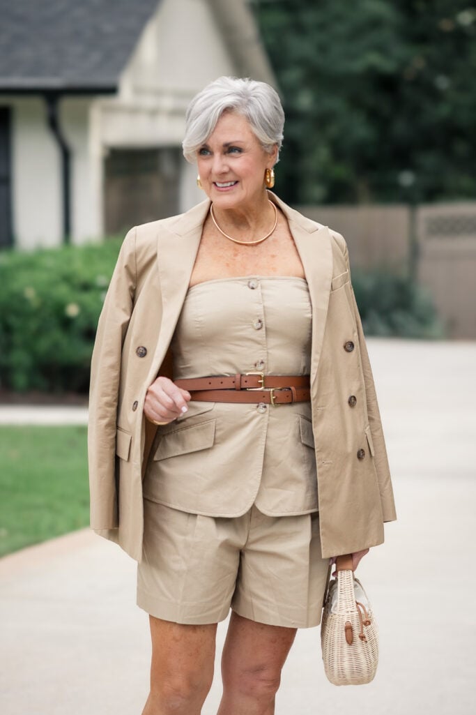Khaki short suit with a double-breasted blazer, leather belt, raffia sandals, and wicker bag