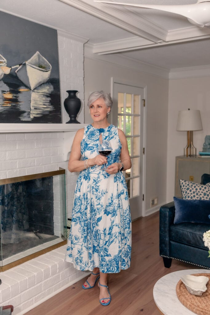 Beth wearing a blue and white floral toile midi dress with blue strappy sandals, photographed at home